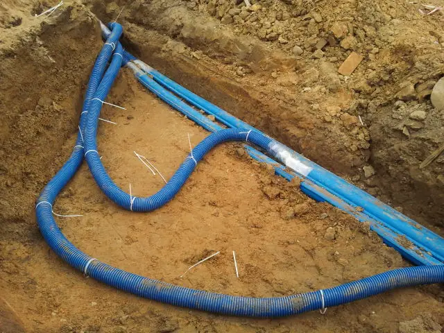 Splot niebieskich rur instalacyjnych połączonych w gnieździe wykopu przed budynkiem