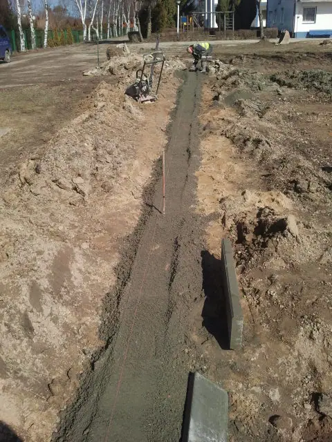 Wąski wykop z betonową ławą fundamentową wzdłuż linii przyszłego ogrodzenia boiska