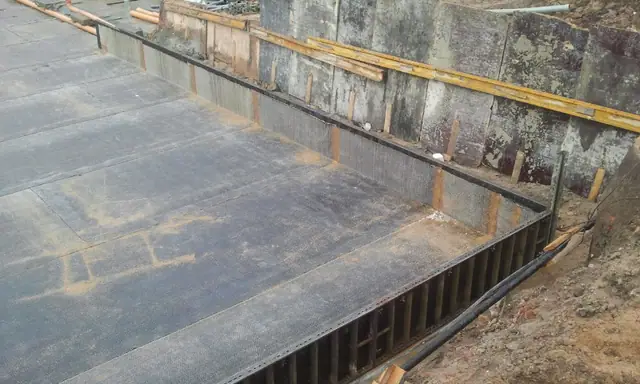 Zbliżenie krawędzi zaizolowanej płyty fundamentowej ze stalowym szalunkiem wykopu