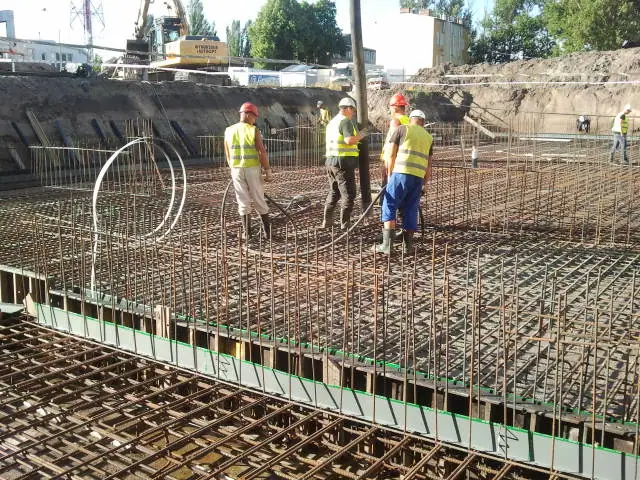 Robotnicy trzymają wąż pompy, rozprowadzając beton po zbrojeniu w promieniach słońca
