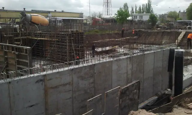 Robotnicy montują stalowe szalunki ścian fundamentowych w wykopie inwestycji Bursztynowe