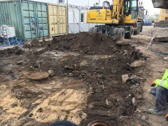 Koparka Komatsu i hałda gruzu obok niebieskich kontenerów magazynowych na budowie