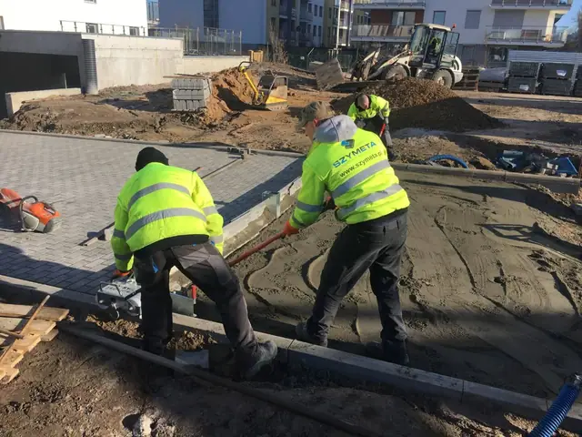 Dwóch robotników firmy Szymeta zagęszcza podsypkę wzdłuż nowo ułożonego krawężnika
