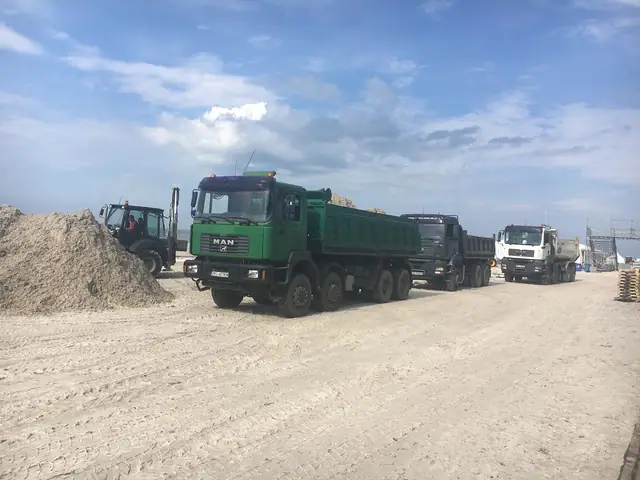 Kolumna samochodów ciężarowych na piaszczystym placu budowy areny Cavaliady w Kołobrzegu