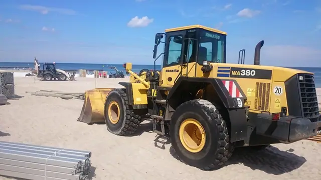 Ładowarka kołowa Komatsu WA380 rozgarnia piasek na plaży podczas przygotowań do Cavaliady w Kołobrzegu