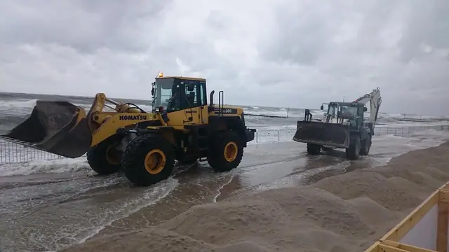 Ładowarka i koparka pracują przy linii brzegowej wśród fal na plaży podczas przygotowań do Cavaliady