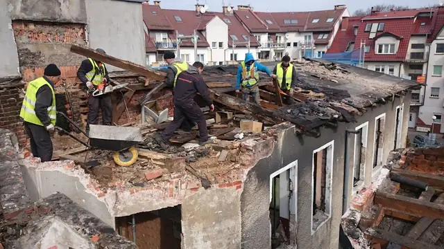 Pracownicy w kaskach ręcznie demontują poszycie dachu podczas rozbiórki kamienicy