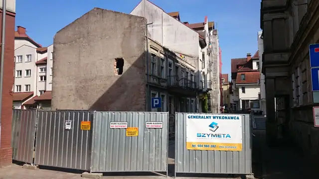 Koparka z młotem hydraulicznym rozbija ceglane ściany zabudowań gospodarczych