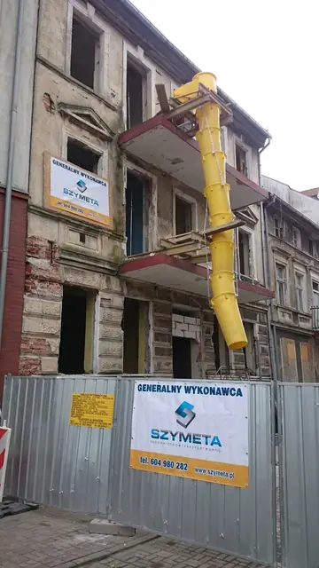 Kolejne ujęcie ramienia wyburzeniowego pracującego przy dachu rozbieranej kamienicy