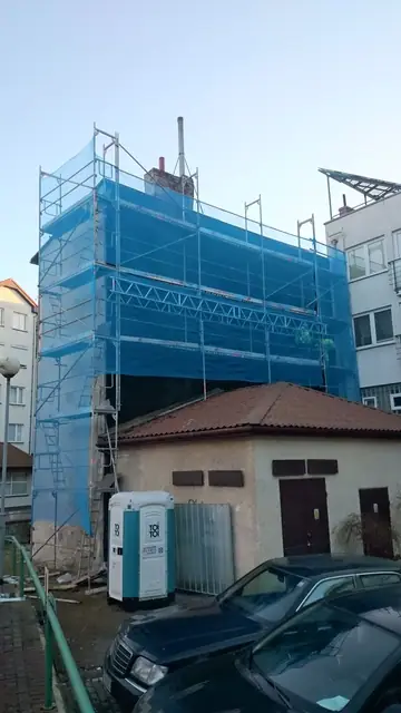 Budynek owinięty niebieską siatką rusztowania w trakcie przygotowań do wyburzenia