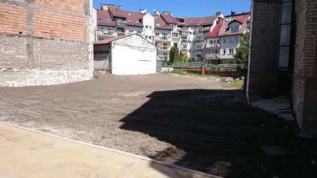 Wyrównany plac po zakończonej rozbiórce z widoczną zabudową mieszkalną w tle
