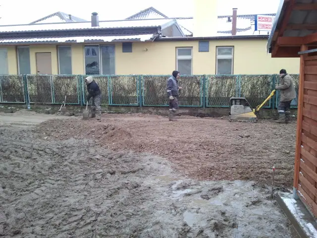 Trzej robotnicy przygotowują podłoże zagęszczarką wzdłuż ogrodzonej granicy działki