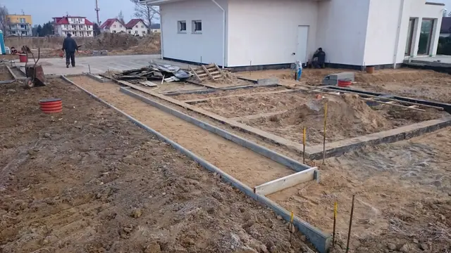 Betonowa opaska fundamentowa wokół domu z widocznymi przyłączami kanalizacyjnymi