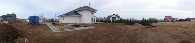 Panorama działki z domem jednorodzinnym w tle i hałdami ziemi na pierwszym planie