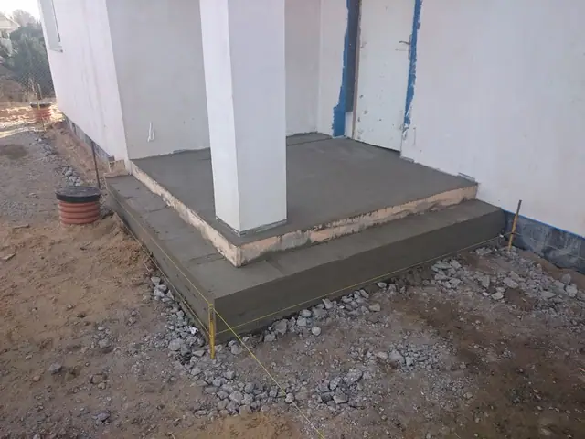Betonowy podest tarasu przy elewacji domu, widoczne zbrojenie wystające ze ściany