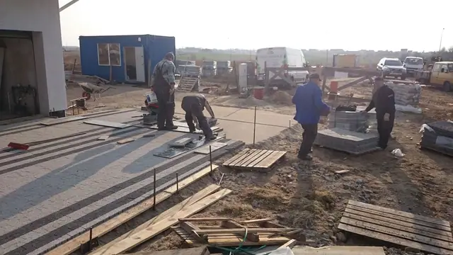 Robotnicy układają kostkę brukową w geometryczny wzór na podjeździe przed domem