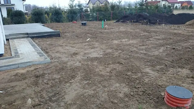 Wytyczony teren pod nawierzchnię z kostki i murek oporowy przy domu, obok kręgi kanalizacyjne