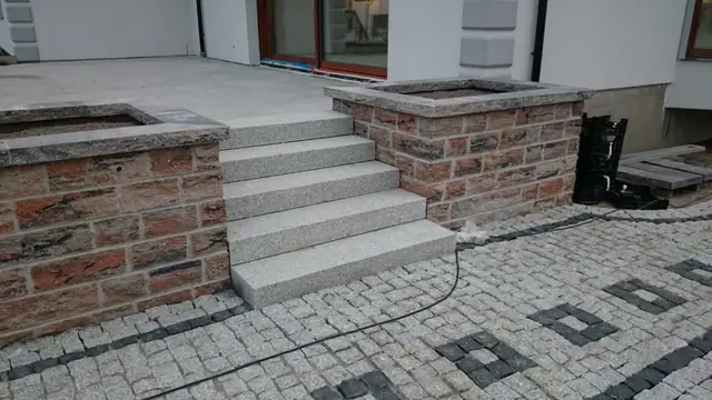 Granitowe schody między dwiema murowanymi donicami prowadzące na taras domu