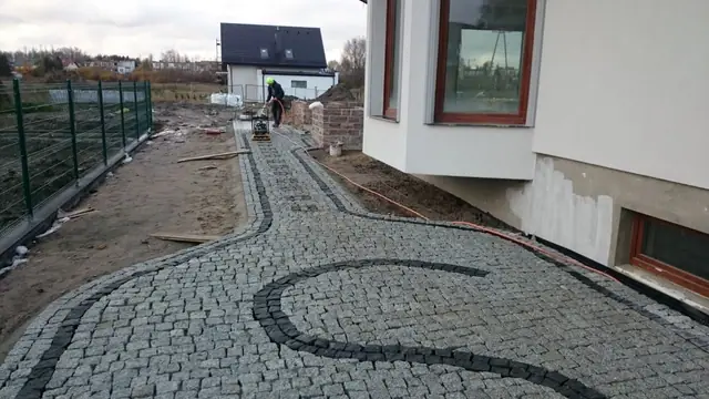 Pracownik układa kostkę brukową na podjeździe wzdłuż ogrodzenia posesji
