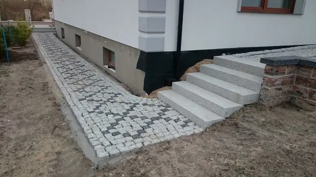 Szeroki widok podjazdu z kostki brukowej w kształcie litery S i kamiennych słupków