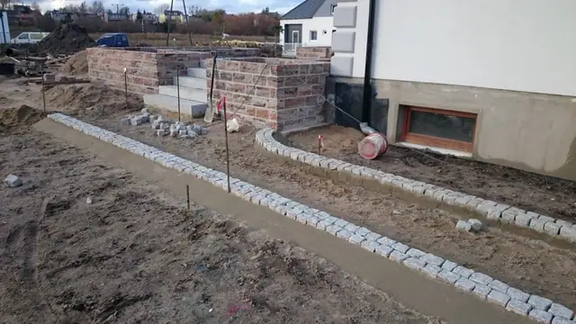 Brukarze kończą ścieżkę z kostki przy murowanych słupkach ogrodzenia domu