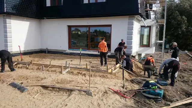 Pracownicy wytyczają sznurkiem linie pod nawierzchnię przy tarasie domu jednorodzinnego