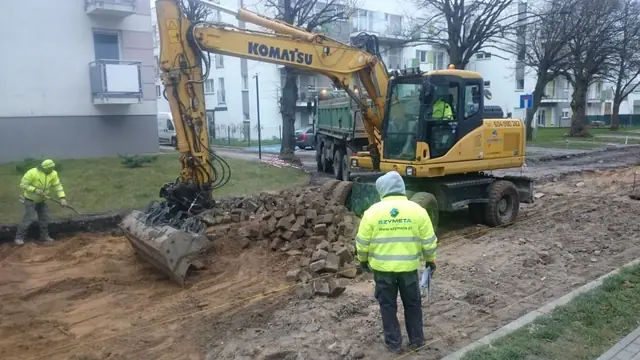 Koparka Komatsu i robotnicy układają krawężnik na rozkopanej drodze wewnętrznej w Kołobrzegu