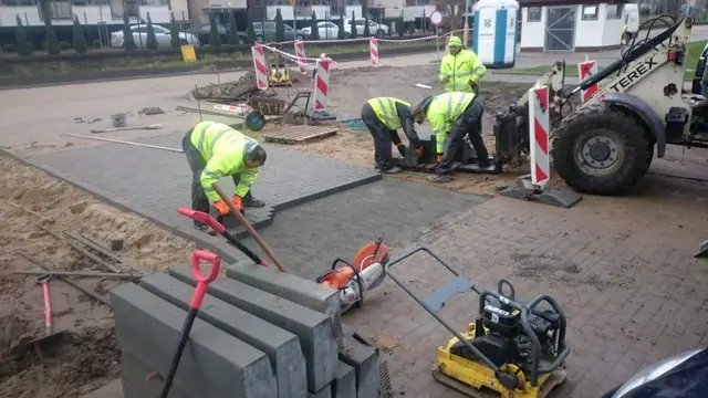 Robotnicy układają kostkę brukową przy krawężniku i obsługują zagęszczarkę na ulicy Wielkopolskiej w Kołobrzegu