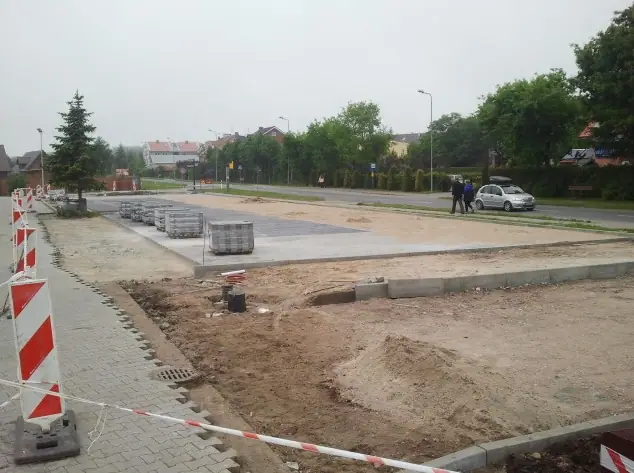 Wykończona betonowa nawierzchnia parkingu obramowana krawężnikiem i barierami ostrzegawczymi