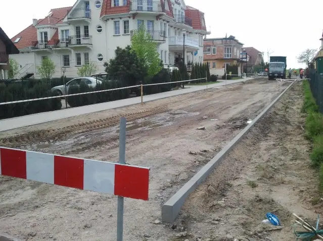 Świeżo osadzony betonowy krawężnik obramowuje żwirową jezdnię przy znaku ostrzegawczym
