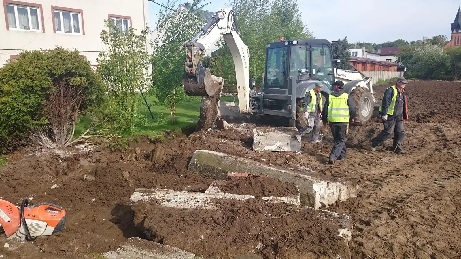 Koparka i robotnicy demontują stary betonowy płot na granicy działki w Ustroniu Morskim