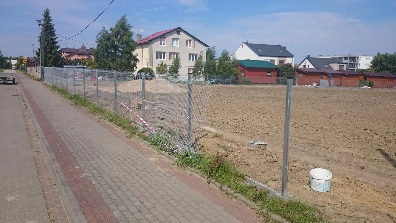 Gotowe ogrodzenie z siatki na słupkach wzdłuż chodnika z czerwonej kostki brukowej
