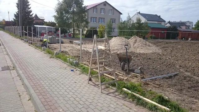 Nowo ułożony chodnik z czerwonej kostki brukowej przy budowanym ogrodzeniu i drabinie malarskiej