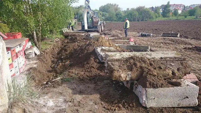 Rozebrane betonowe przęsła starego ogrodzenia leżą na ziemi obok skrzynek po roślinach