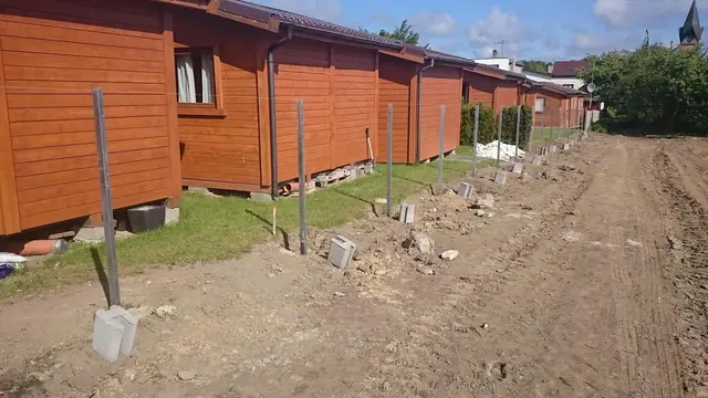 Rząd nowo osadzonych stalowych słupków ogrodzeniowych wzdłuż drewnianych domków letniskowych