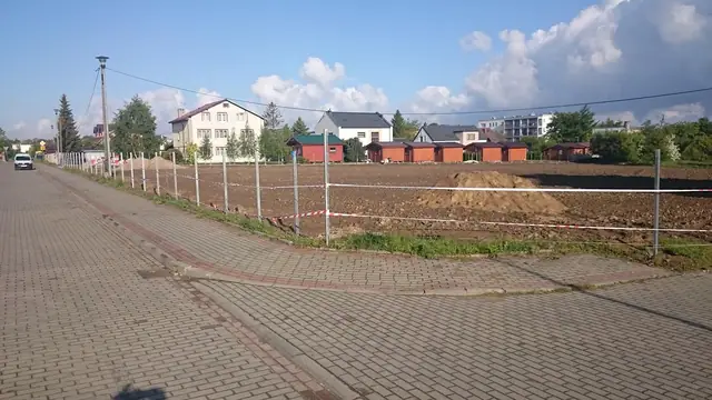 Siatkowe ogrodzenie z napiętym drutem wzdłuż chodnika z kostki brukowej przy zabudowie