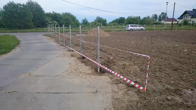 Taśma ostrzegawcza rozciągnięta pomiędzy słupkami nowego ogrodzenia przy drodze wewnętrznej