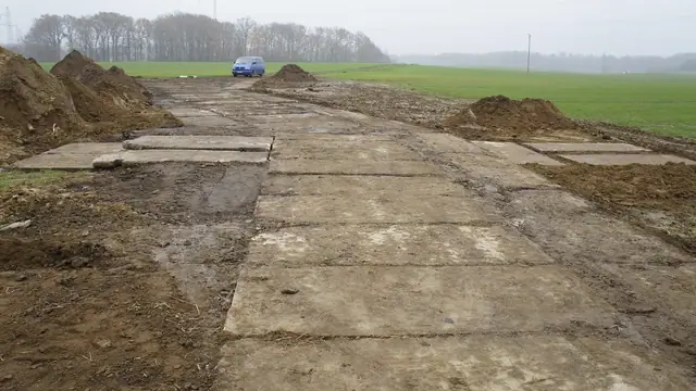 Droga z płyt betonowych wśród pól uprawnych z zaparkowanym samochodem w tle