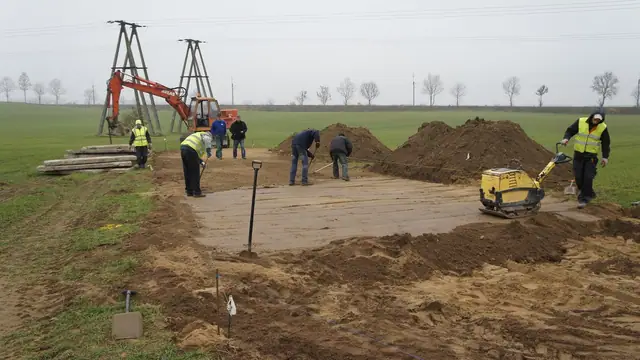 Ekipa układa płyty drogowe pod masztami linii energetycznej i zagęszcza podłoże