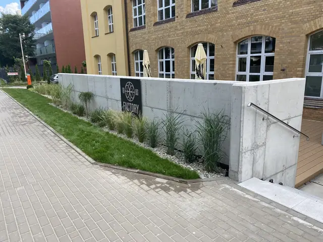 Narożnik zagłębionego tarasu z logo Factory Resort umieszczonym wśród ozdobnych traw