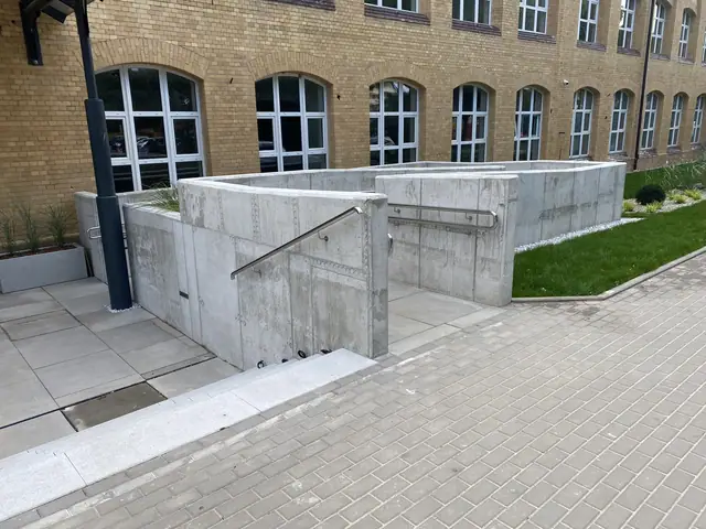 Szerszy widok betonowych ścian zagłębionego tarasu ze stalowymi poręczami i nową nawierzchnią
