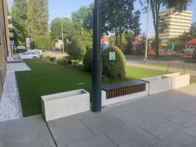 Zagospodarowany trawnik z latarnią, drewnianą ławką i obrzeżem żwirowym przy wejściu
