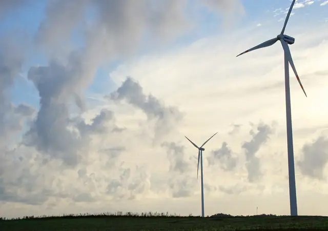 Turbina wiatrowa na tle ciemnych, burzowych chmur nad polem uprawnym