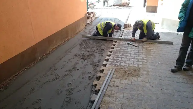 Robotnicy zacierają świeżo wylaną wylewkę betonową przy ścianie budynku