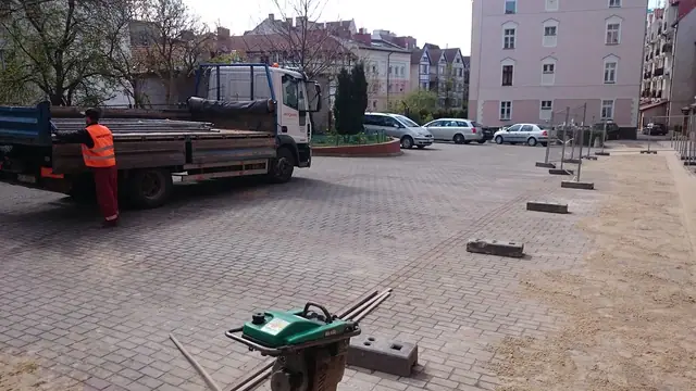 Robotnik prowadzi zagęszczarkę po nowo ułożonej kostce, w tle ciężarówka dostawcza