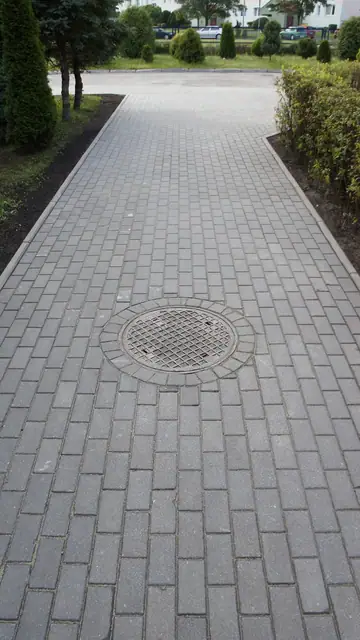 Prosty chodnik z szarej kostki brukowej ze studzienką kanalizacyjną na terenie szkoły