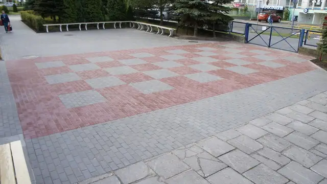Plac przed szkołą wyłożony kostką w biało-czerwoną szachownicę, ławki wzdłuż ogrodzenia