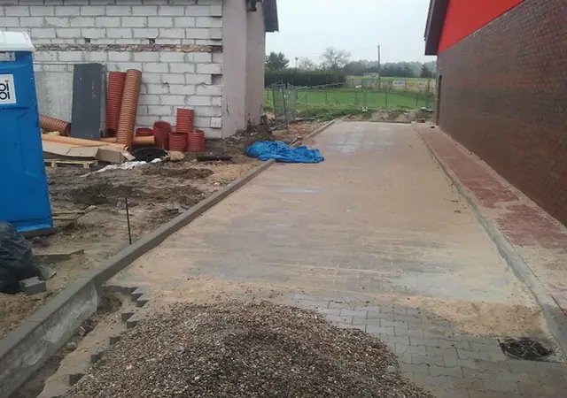 Wąski chodnik z kostki brukowej wzdłuż ściany budynku z czerwonej cegły, obok kontener na gruz