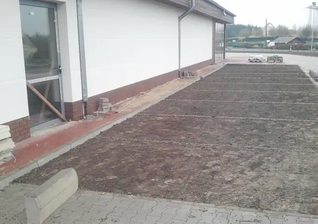 Świeżo utwardzony pas ziemi przy elewacji budynku marketu z betonowym obrzeżem