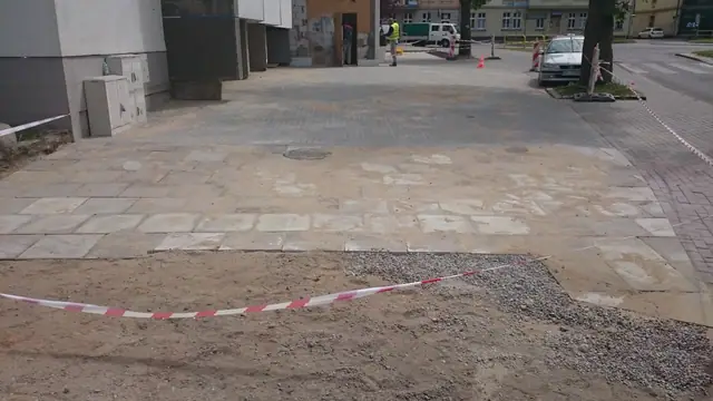 Fragment nowej nawierzchni z kostki brukowej odgrodzony taśmą od żwirowego podłoża przed wejściem